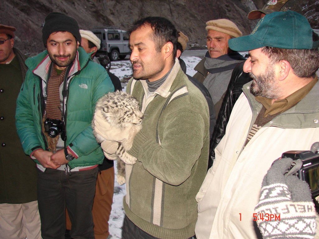 Man holding snow leopard cub with other men around him